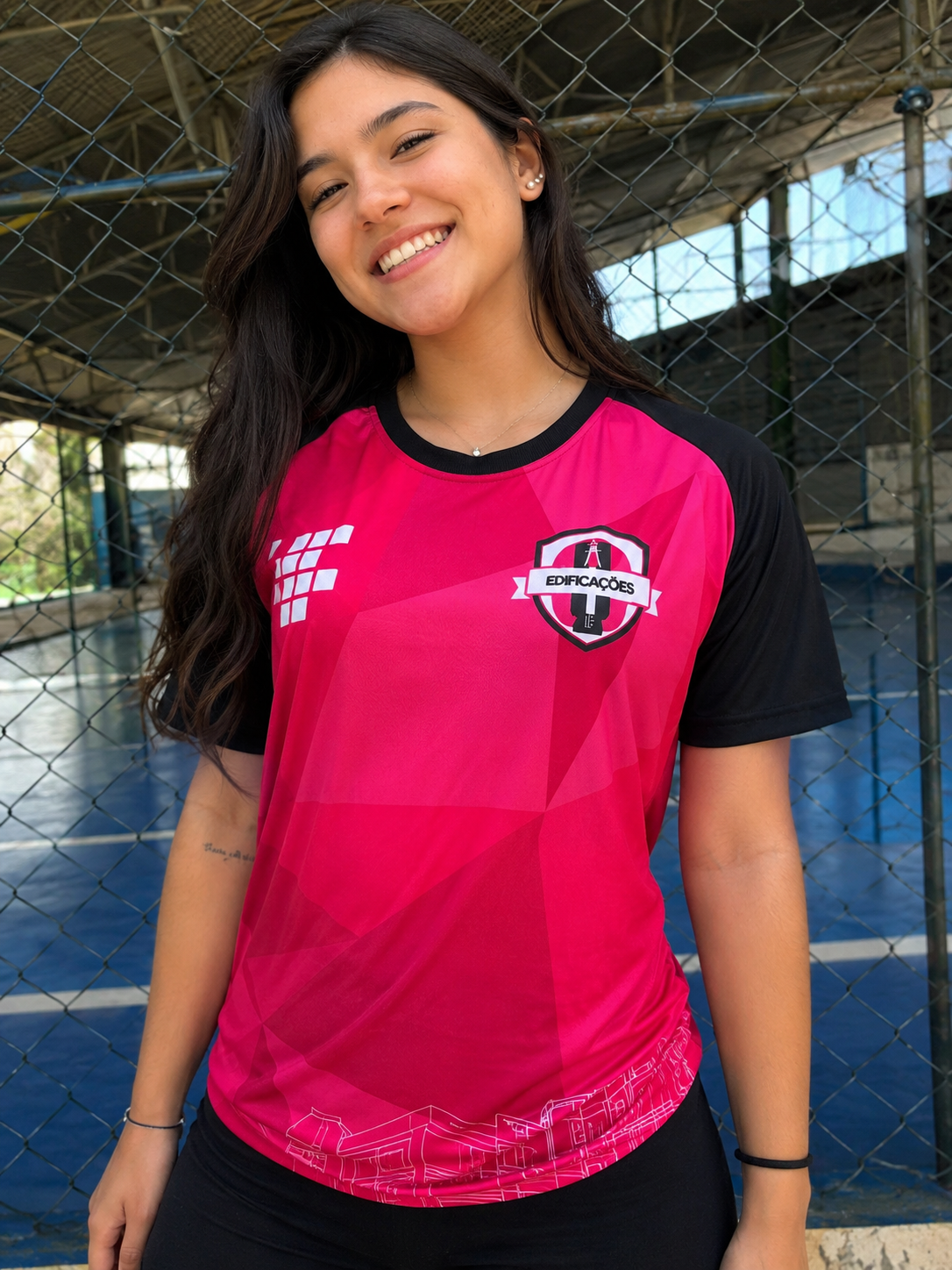 Jovem sorrindo vestindo camisa rosa com mangas pretas para interclasse Edificações